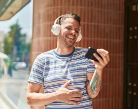 Hombre escuchando música y viendo un video en tu teléfono mientras ríe