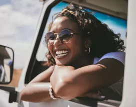 Chica sonriendo mirando por la ventana de un auto en movimieno, disfrutando de su viaje